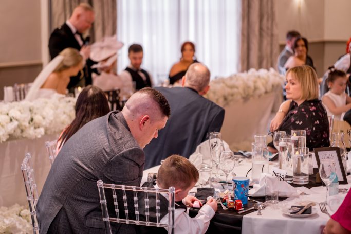 Guests seated at a wedding reception, some attentive and others engaged in conversation.