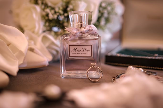 A glass perfume bottle with a bow, surrounded by white flowers and elegant accessories.