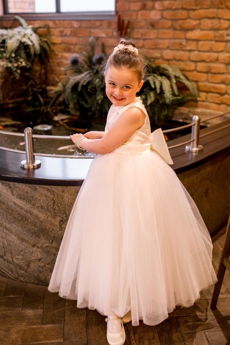 Smiling young girl in a white dress poses by a decorative fountain.
