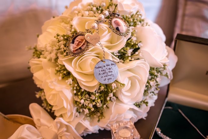 A wedding bouquet featuring white roses, lace, and decorative charms.