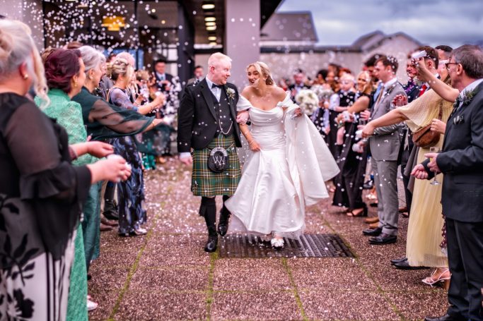 Bride and groom walking through a celebratory archway of guests at a wedding.