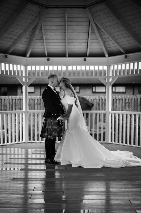 A bride and groom stand in a gazebo, sharing a moment together.