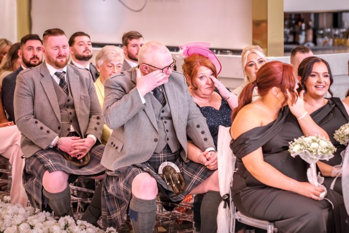 Guests seated at a wedding, some visibly emotional, wearing formal attire.