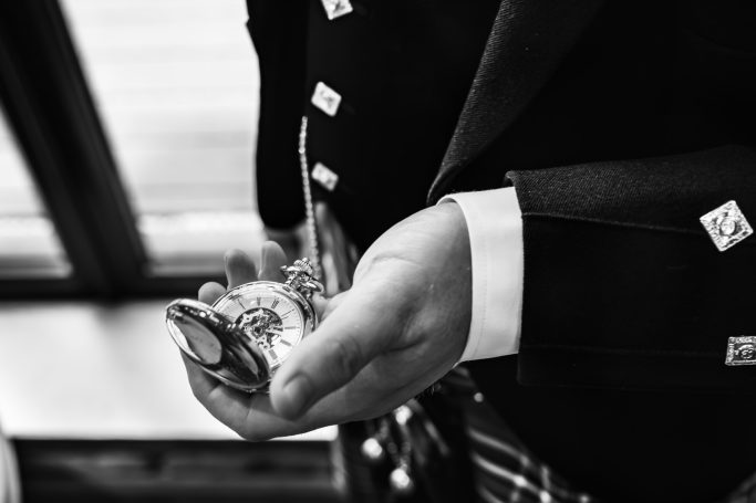 A person in a suit holds a silver pocket watch, with a blurred background.