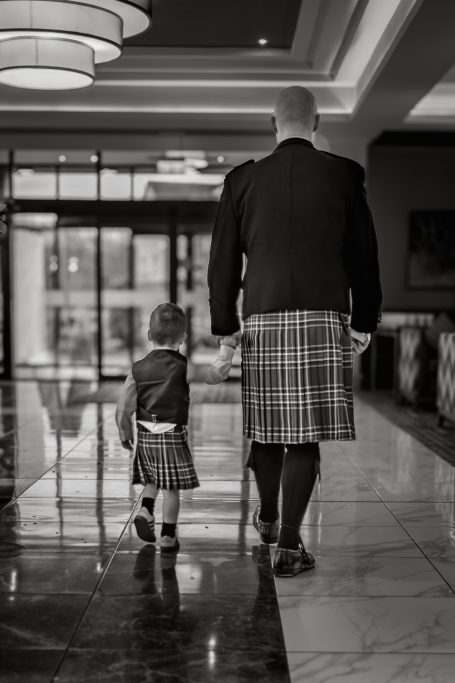 A man and a child in kilts walk hand in hand through a hotel lobby.